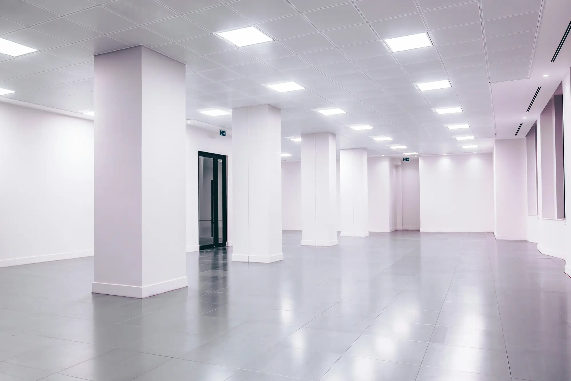 An empty, light-filled room with white walls, columns and a black door.