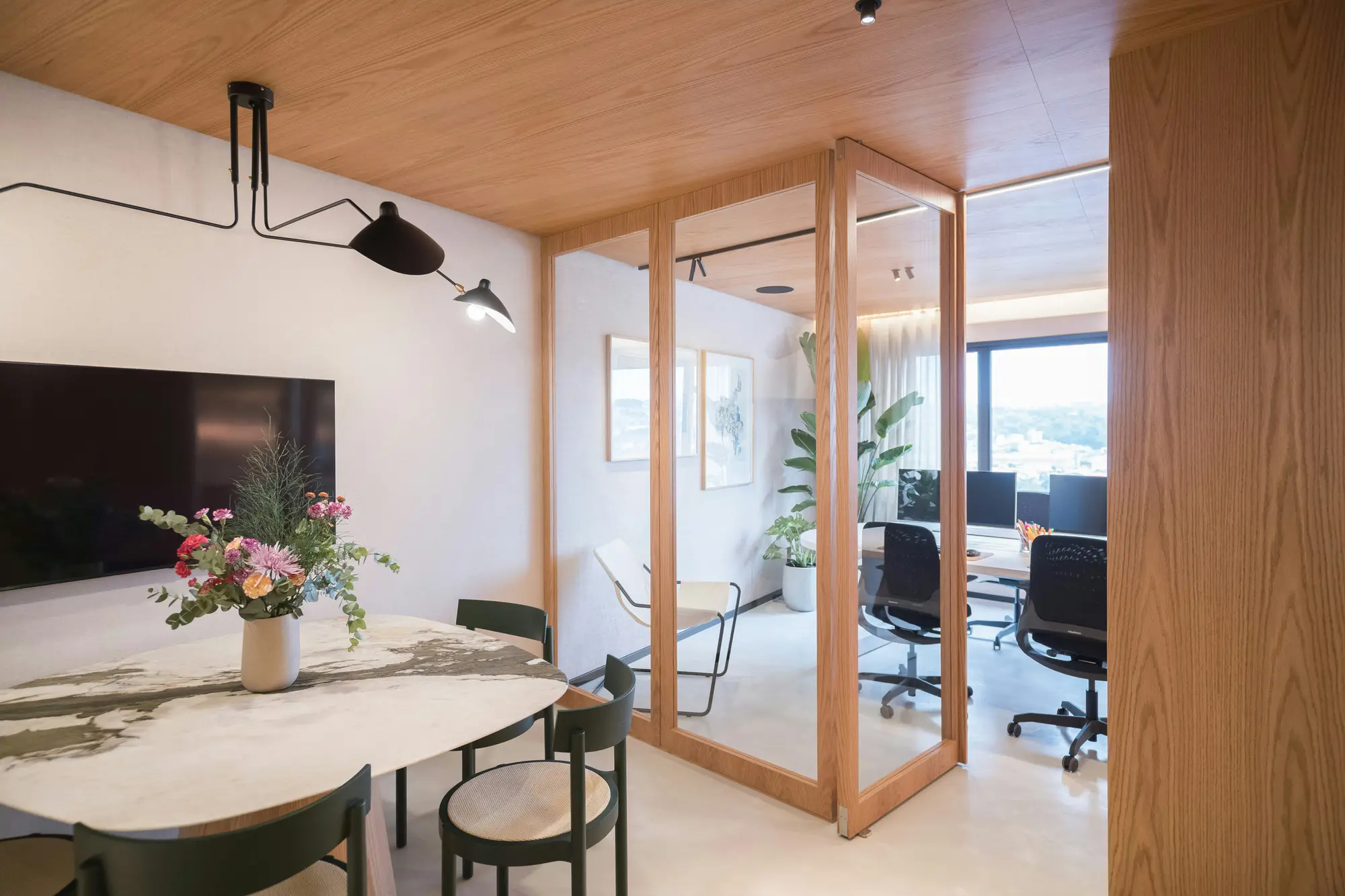 A warm, wood-panelled modern office with a meeting area and workstations beyond a glass partition.